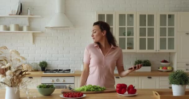 Mutlu kaygısız ev hanımı mutfakta yemek pişirirken müzik dinlesin. — Stok video