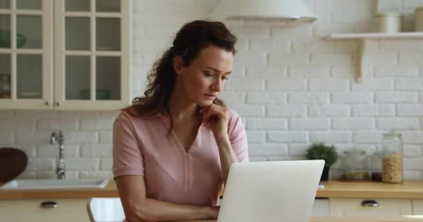 Femme coûteuse sérieuse travaillant sur un ordinateur portable dans la cuisine — Video