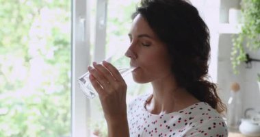 Su içen genç, mutlu kadın, pencerenin yanında duruyor..