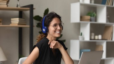 Kulaklıklı çok neşeli genç bir kadın dizüstü bilgisayarla çalışıyor.