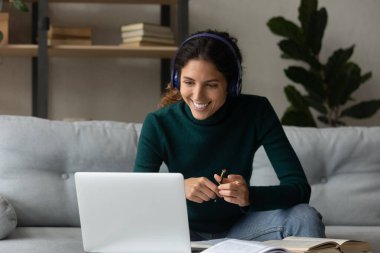 Kulaklıklı gülümseyen kadın evdeki bilgisayarda çalışıyor.