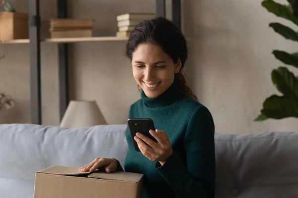Uśmiechnięta kobieta rozpakować pudełko zakupy na smartfonie — Zdjęcie stockowe