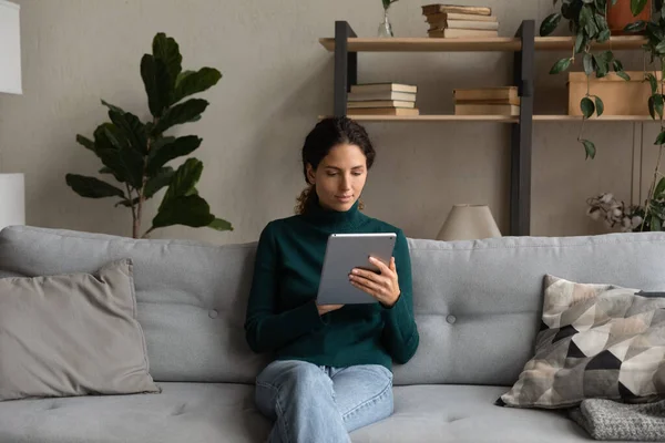 Mujer joven sentada en el sofá usando gadget tableta — Foto de Stock