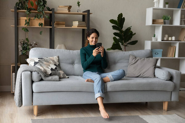 Happy young woman sit on sofa talk on smartphone