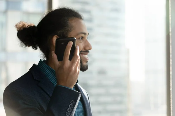 Empresário étnico sorridente usa alto-falante na célula moderna — Fotografia de Stock