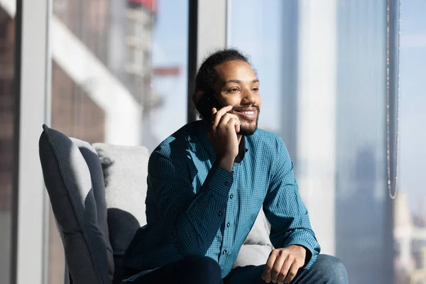 Sonriente hombre étnico utilizar el teléfono celular hablando con el cliente —  Fotos de Stock