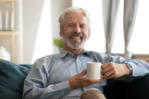 Счастливый зрелый мужчина отдыхает на диване с кофе в руках. — стоковое фото