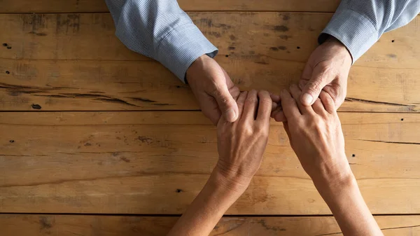 Compassionate middle aged man holding wrinkled hands of elderly woman. — Stock Photo, Image