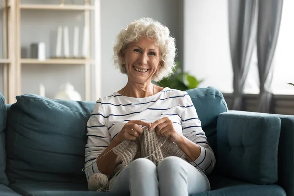 Retrato de anciana sonriente tejiendo ropa de abrigo en casa. — Foto de Stock