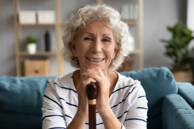 Gülümseyen yaşlı beyaz bir kadının portresi. Elinde tahta bir sopa..