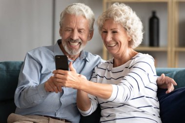 Gülümseyen olgun, yaşlı, evli bir çift akıllı telefon kullanıyor..