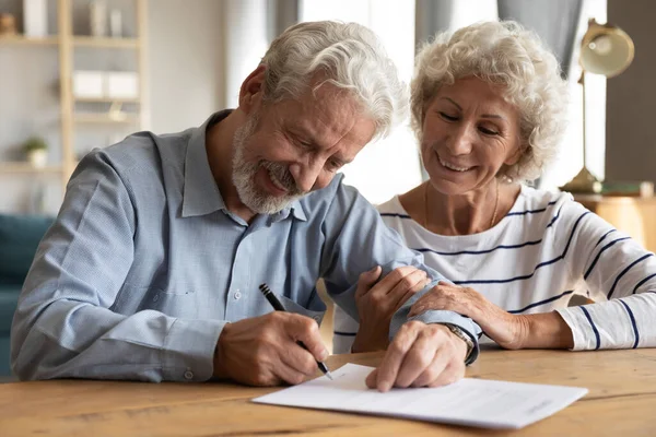 Happy old mature retired family couple putting signature on paper document.