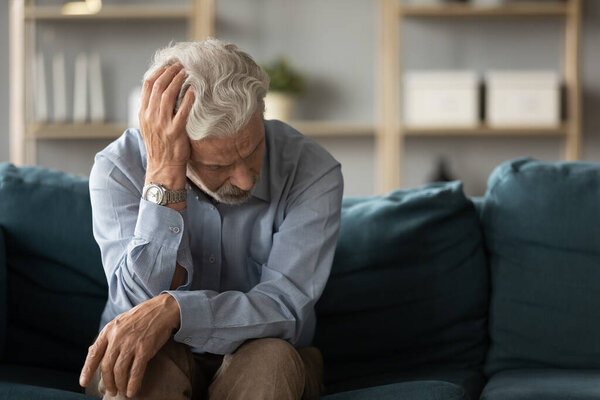 Frustrated unhappy middle aged mature man sitting on sofa.