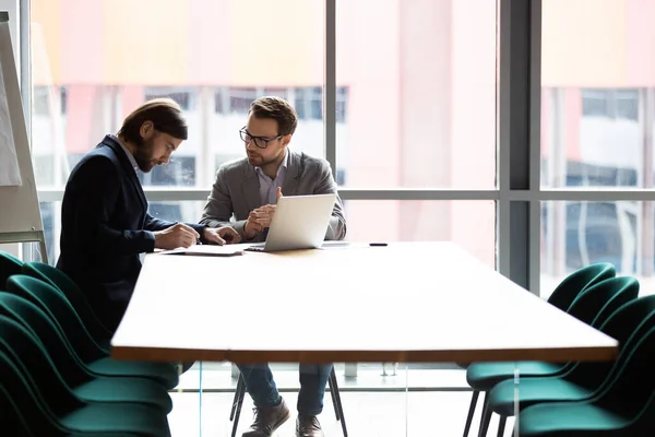 Twee zelfverzekerde mannelijke partners ondertekenen overeenkomst tijdens onderhandelingsvergadering. — Stockfoto