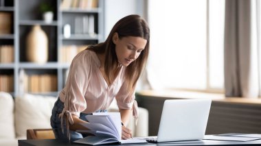 Kendine güveni tam bir iş kadını. Not defterine yazıyor. Çalışma masasında duruyor.