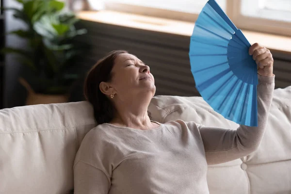 Крупним планом виснажена жінка середнього віку махає паперовим вентилятором — стокове фото