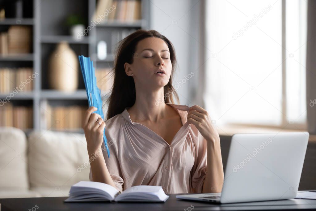 Close up thirsty woman waving paper fan, sitting at desk