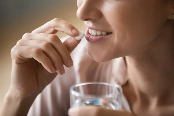 Close up smiling woman holding pill and glass of water — Stock Photo, Image