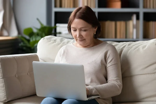 Laptop kullanan, koltukta oturan olgun bir kadını kapat. — Stok fotoğraf