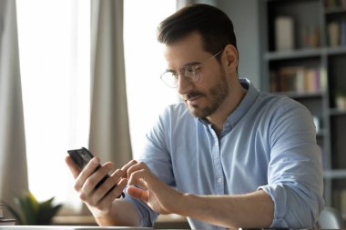 Mutlu gülümseyen milenyum adamı evde akıllı telefon uygulamaları kullanıyor..