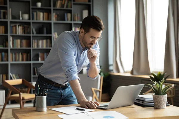 Jeune homme d'affaires réfléchi travaillant sur ordinateur debout à la table. — Photo