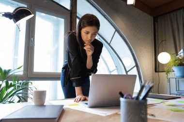 Düşünceli Hintli iş kadını yönetici çeneye dokunuyor, laptop ekranına bakıyor.