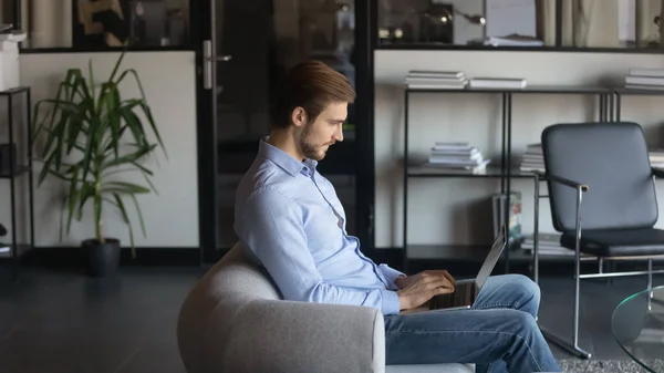 Bilgisayarı kullanan, modern ofiste koltukta oturan kendine güvenen bir iş adamı. — Stok fotoğraf