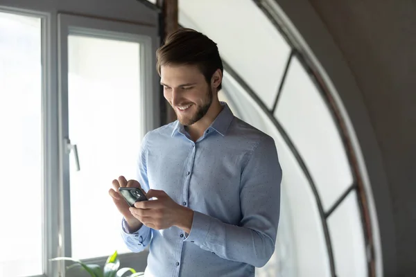 Zblízka usměvavý podnikatel pomocí chytrého telefonu, stojící v úřadu — Stock fotografie