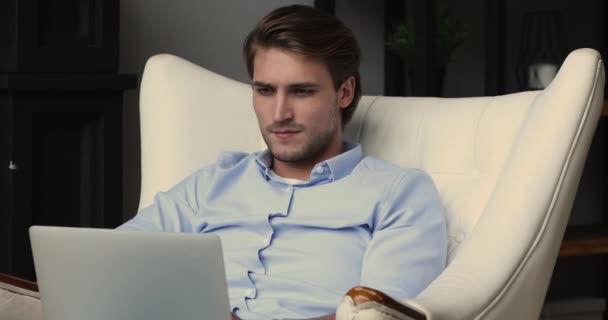 Gericht millennial knappe zakenman werken op computer zitten in fauteuil. — Stockvideo