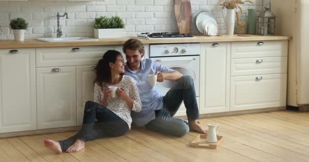 Relaxado jovem casal sentado no chão quente de madeira na cozinha. — Vídeo de Stock