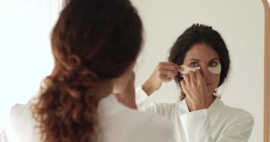 Güzel genç bir kadın göz altı bölgelerine nemlendirici bantlar yapıştırıyor..