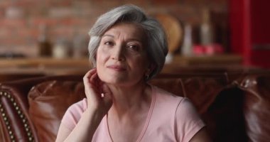 Çekici, olgun bir kadın. Kanepeye otur ve kameraya bak.