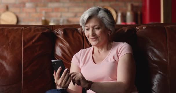 年上の女性は、スマートフォンで自宅で快適なソファに休んで — ストック動画