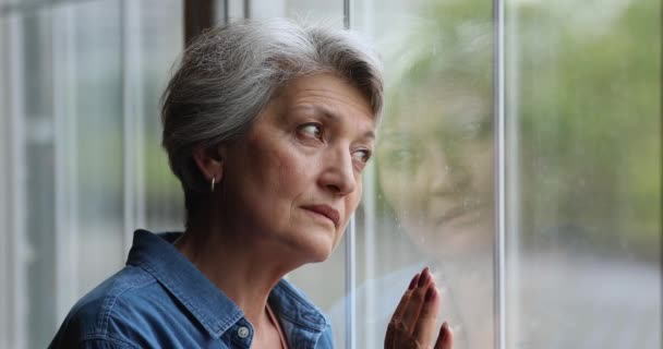 窓の近くに立って悲しい年上の女性は外に見える落ち込んでいる — ストック動画