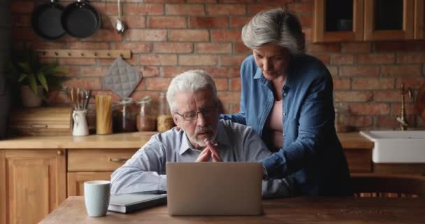 讨论网上购物的年长配偶在厨房里使用笔记本电脑 — 图库视频影像