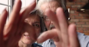 Birleştirilmiş parmaklarıyla kalp şekli veren yaşlı çift yüzleri.