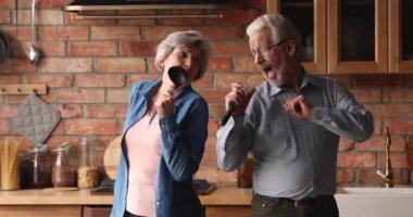 Yaşlı eşler dans edip şarkı söylüyor ve modern mutfakta birlikte eğleniyorlar.