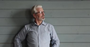 Stüdyoda ahşap duvarda poz veren yaşlı bir adam.