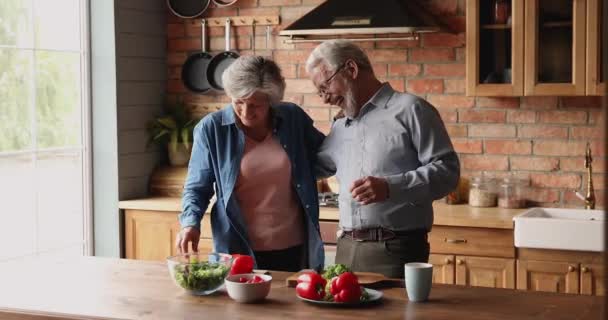 Fröhliche ältere Eheleute lachen beim Salatkochen in der Küche — Stockvideo