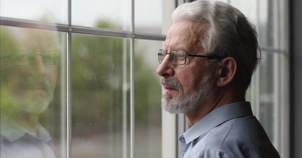 Oudere attente man die binnen uit het raam kijkt — Stockvideo