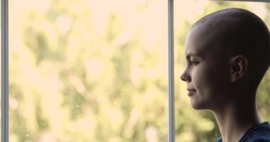 Üzgün kadın kanser hastası içeride tek başına pencereden dışarı bakıyor.