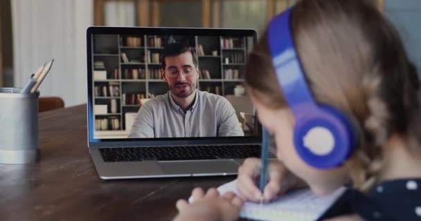 Вид через плечо ребенка сидеть за столом слушает онлайн учитель — стоковое видео