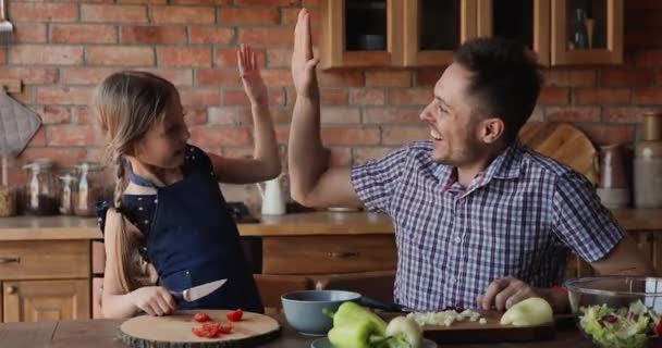 Kleine dochter geeft vader high five gebaar tijdens het bereiden van salade — Stockvideo