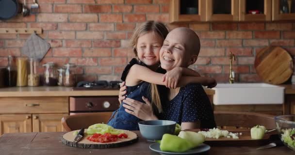 Syg skaldet kvinde omfavne yndig lille datter i køkkenet – Stock-video