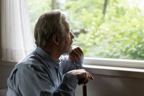 Close up thoughtful mature man holding cane, looking out window