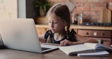 Küçük sevimli kız evde dizüstü bilgisayar kullanarak ders çalışıyor.