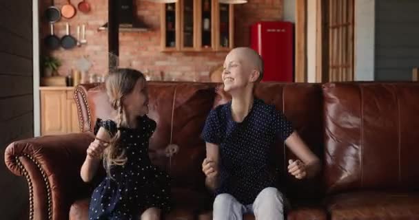 Skallig mor sin dotter lurar tillsammans hoppar sittande på soffan — Stockvideo