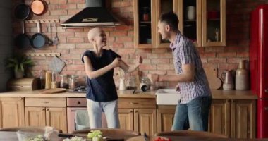 İyimser kadın kanser hastası kocasıyla mutfakta dans ediyor.