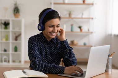 Kulaklık takan Hintli kadın dizüstü bilgisayarın yanına oturur ve internetten ders seçer.