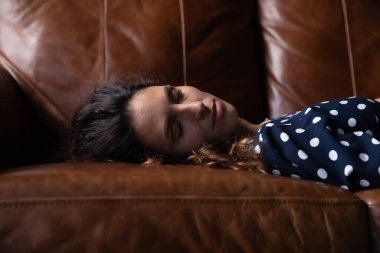 Yorgun genç bir kadın evdeki kanepede uyuyor.